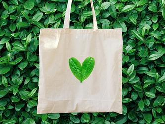 Shopping bag with green leaves shaped as heart against a backdrop of foliage